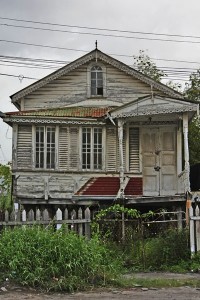 An abandoned old home displays the ornamental touches and shuttered windows of a by-gone era. Its upper window is a common sight on traditional wooden homes