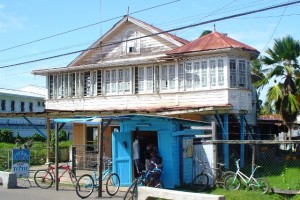 An older home in Berbice showing traditional decorative ventilation designs above once commonly used windows, with a more recent ground floor housing a small shop