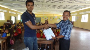 Dr. Khan (left) handing over teaching material to the Kurupukari Primary School headmaster