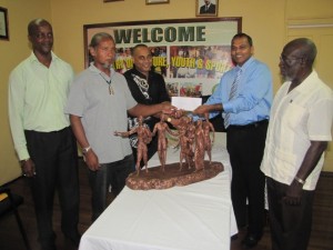 Culture, Youth and Sport Minister Dr Frank Anthony hands over the cheque to sculptors Philbert Gajadhar and Winslow Craig as Director of Culture Dr James Rose and Permanent Secretary Alfred King look on