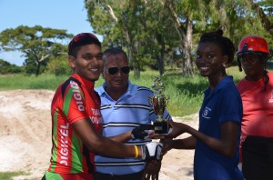 All smiles! A beaming Alanzo Greaves receives the winner’s trophy and prime prize from Customer Service Representative of Hand-in-Hand Insurance Limited, Bonicka Gordon, in the presence of national coach Hassan Mohamed