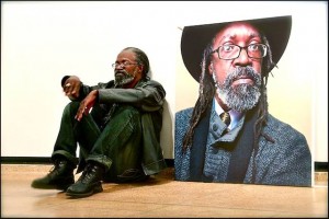 Hazlewood relaxes next to his self-portrait on exhibition at Aljira (Photo by Arlington Weithers)