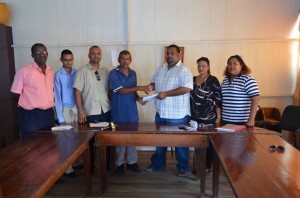 Chairman of the Eccles/Ramsburg Neighbourhood Democratic Council (NDC) Saeed Khan (fourth left) handing over the MoU to Chairman of the Providence Community Center and Sport Club ground and Management Committee Rohan Sarjoo in the presence of NCD councilors, staff and other members of the committee