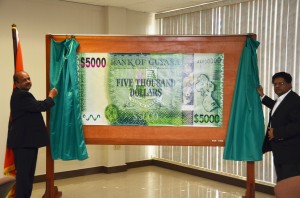 Finance Minister, Dr Ashni Singh (right) assists Bank of Guyana Deputy Governor Dr Gobind Ganga in unveiling the new $5000 note. The new note will go into circulation on December 9