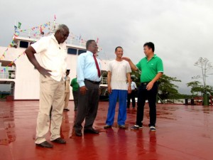 Prime Minister Samuel Hinds and Minister of Public Works  Robeson Benn with owner of the Zhanghao Shipyard, Shuzairong Su and a worker on the deck of the Zhango Hao No. 1.